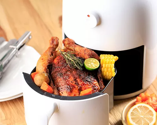 Air Fryer branca com o cesto aberto mostrando um frango assado que acabou de ser preparado.